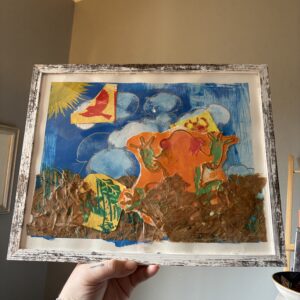 The image shows a framed artwork featuring bright colors with an abstract design, including a large orange frog in the center surrounded by blue and yellow areas with other creatures blended into the collage. The top of the collage includes clouds and a sun. The lower part of the piece is textured paper resembling leaves. The frame is white with a distressed finish.